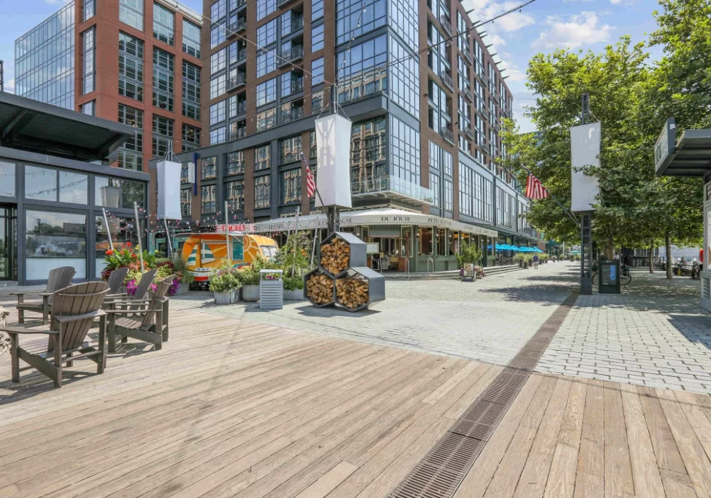 Outdoor plaza with modern buildings, chairs, a colorful kiosk, and stacked firewood on a sunny day.