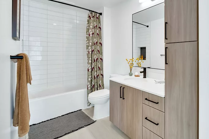 Bathroom with floral shower curtain, wood cabinets, and white tile bathtub surround.